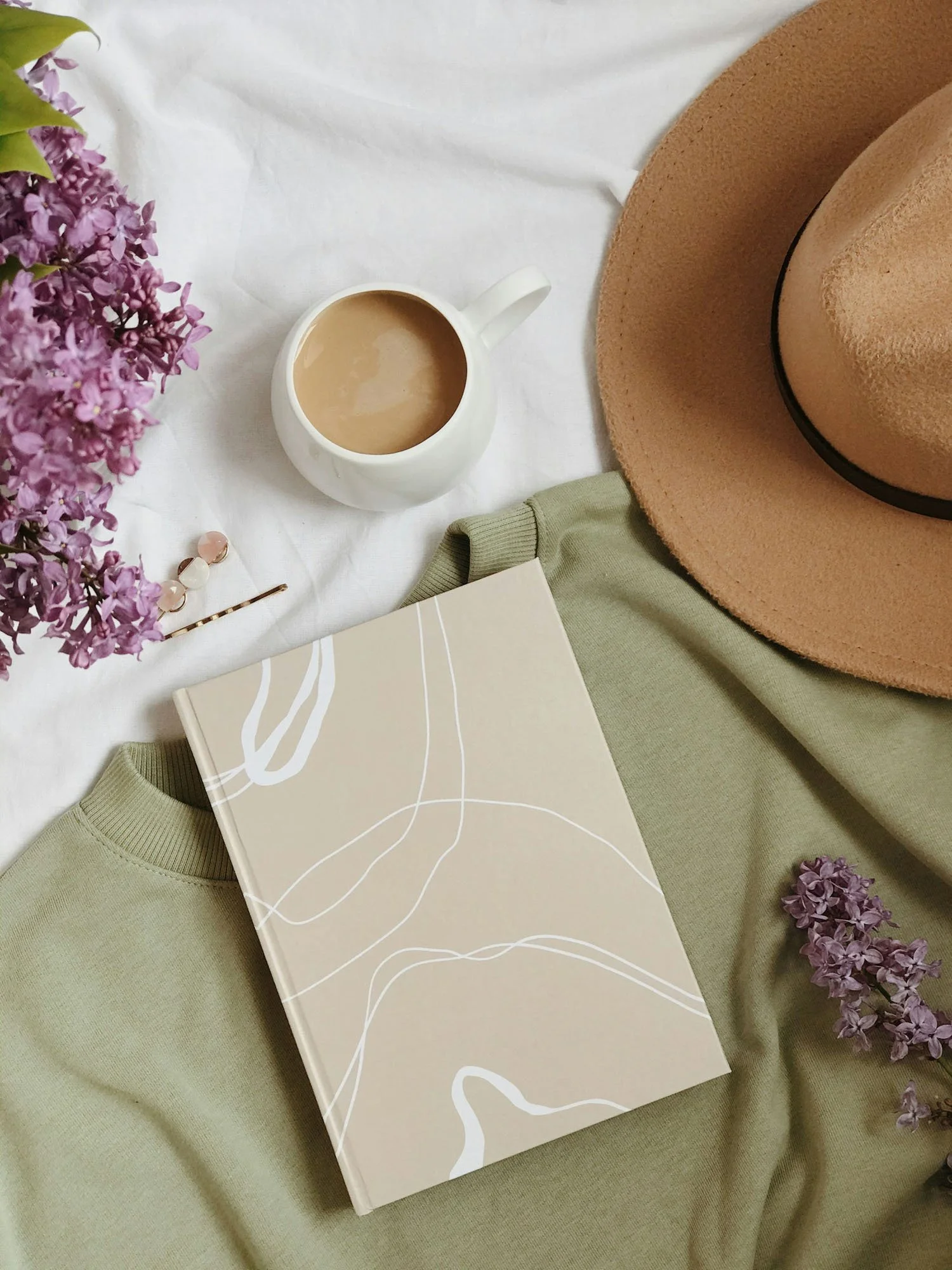 Flat-lay of lilac flowers, coffee mug, journal and lifestyle items
